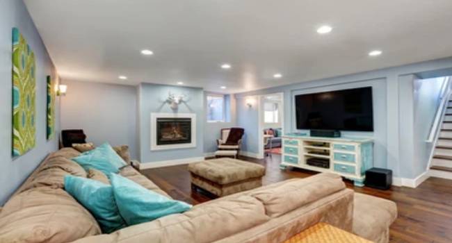 Beautiful Interior of A Living Room In The Unfinished Basement Area With Large Corner Sofa With Blue Pillows And Vintaage TV Cabinet.