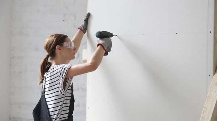 Female home contractor drilling screw holes in drywall