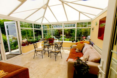 A light and airy furnished sun room (conservatory) with view of trees in the background