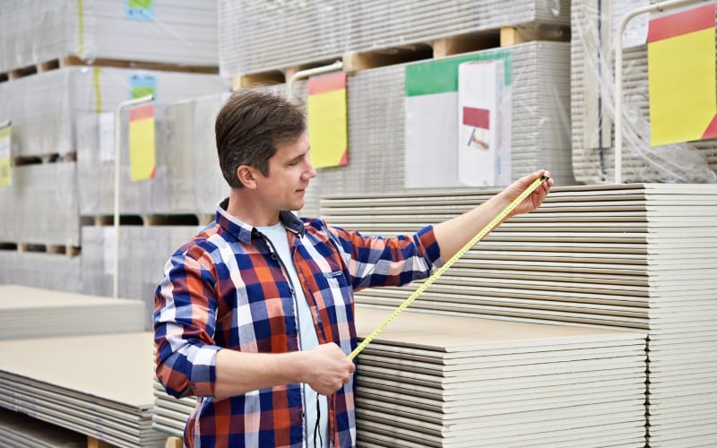 man measures with roulette drywall sheets in store building mate